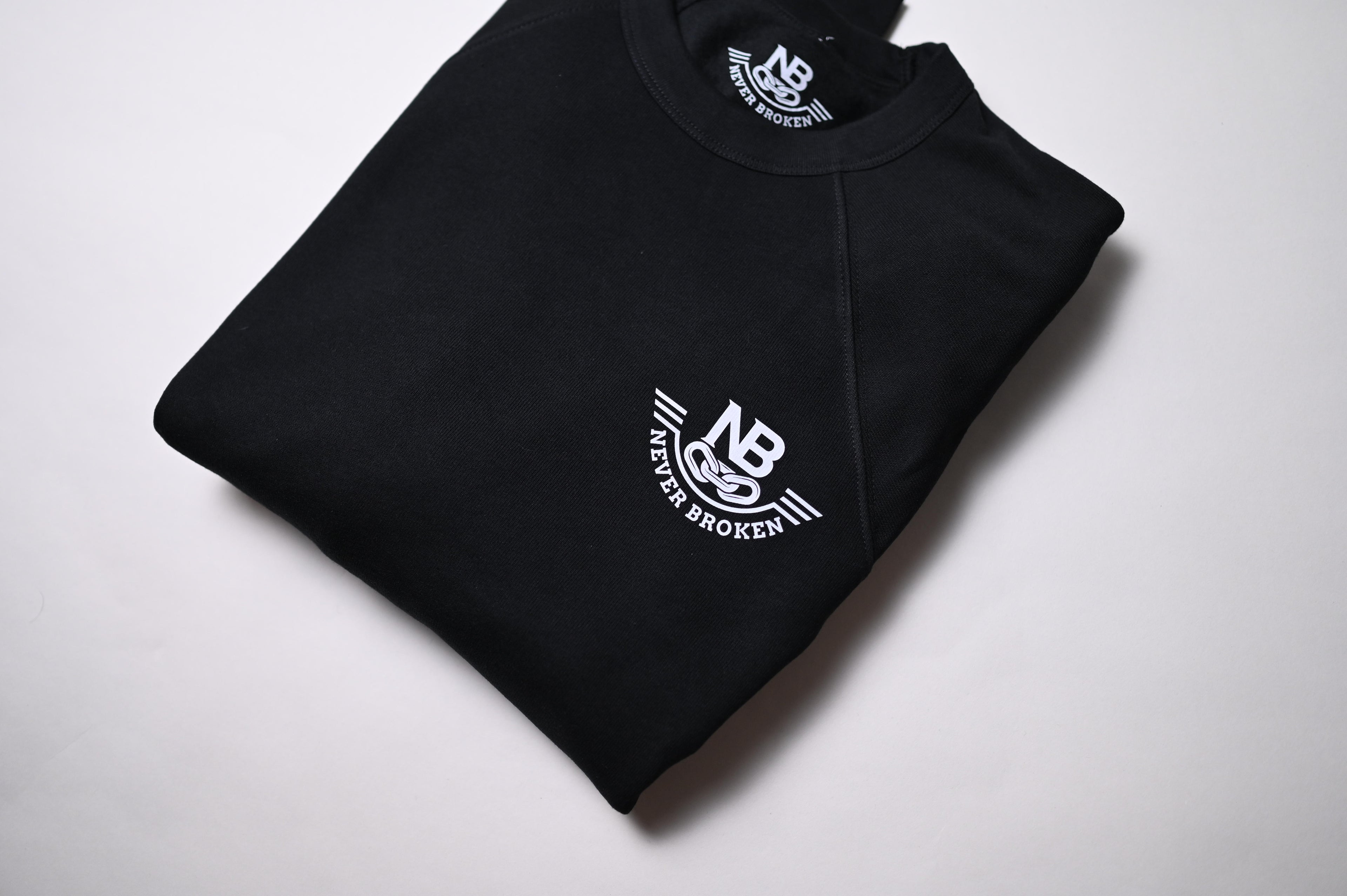 Folded black sweatshirt with 'Never Broken' logo on a white background