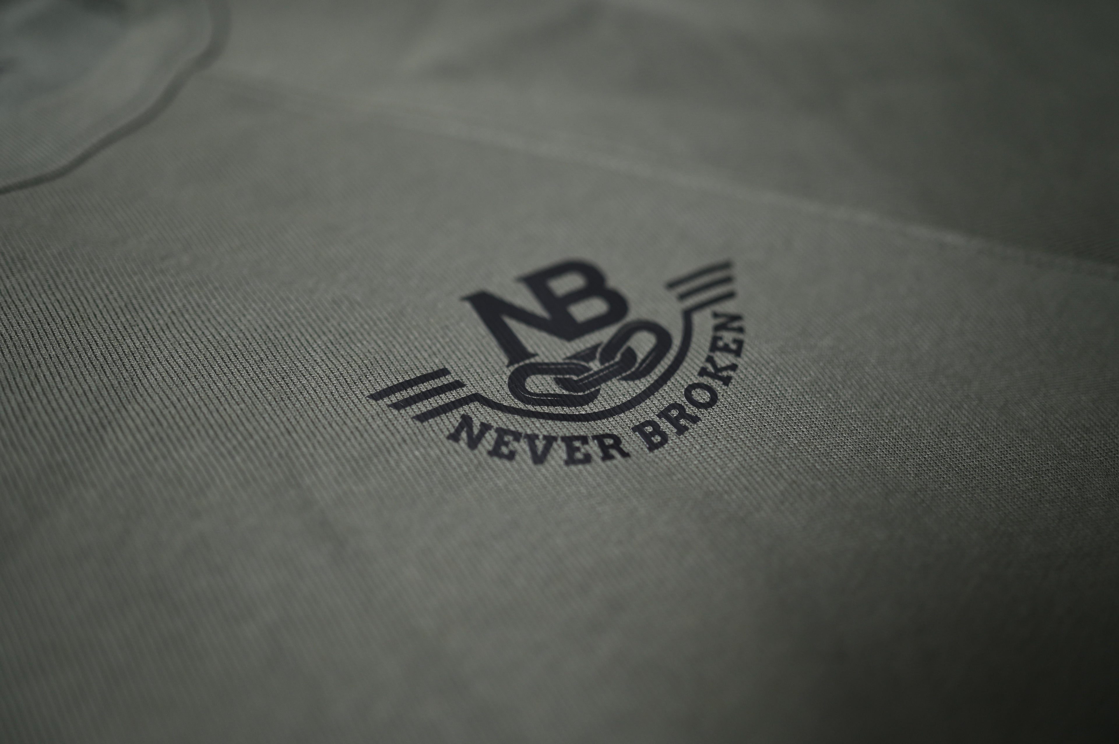 Close-up of a gray fabric with 'Never Broken' logo embroidered on it.
