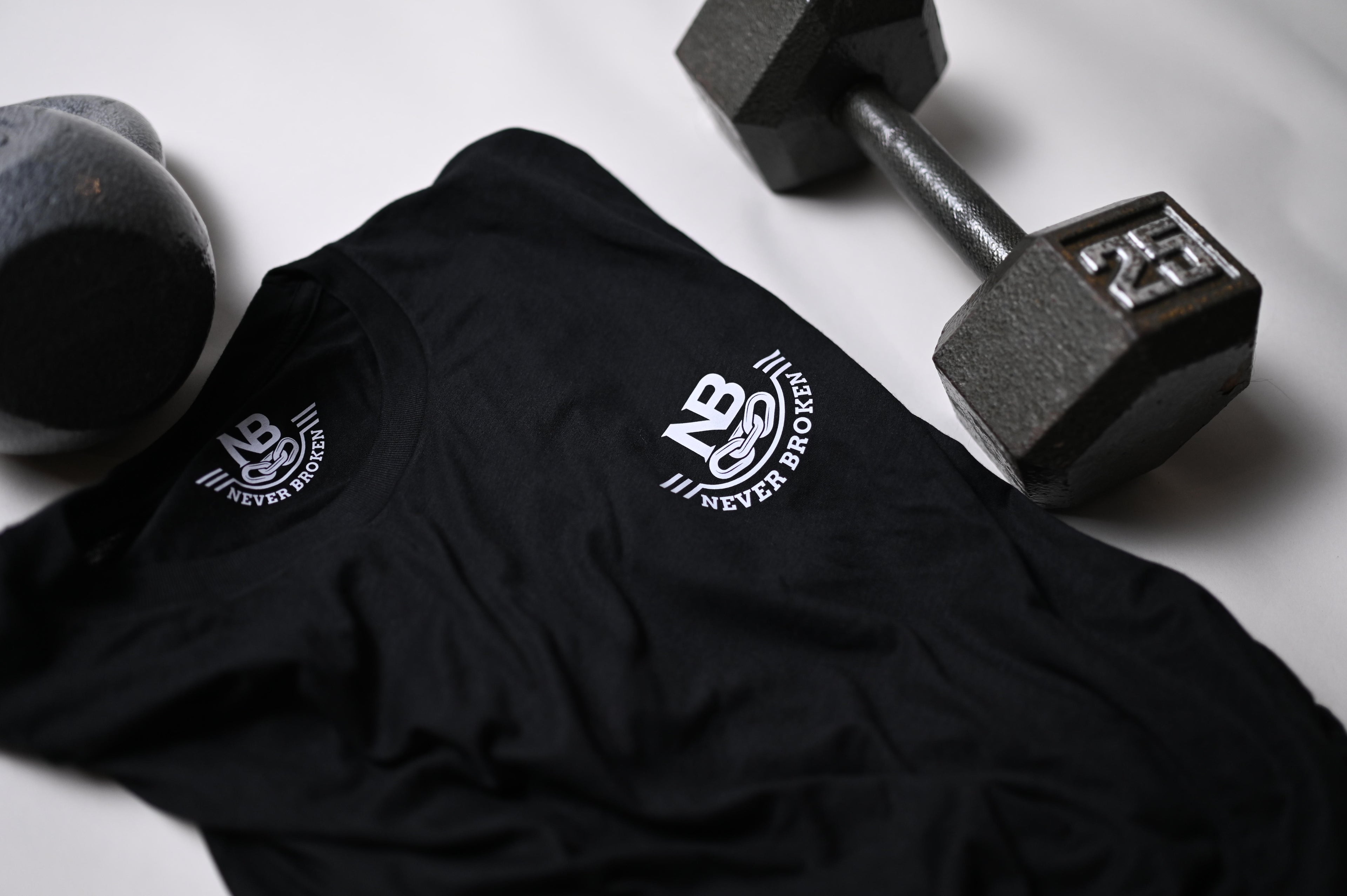 Black t-shirt with a logo and two dumbbells on a light gray background