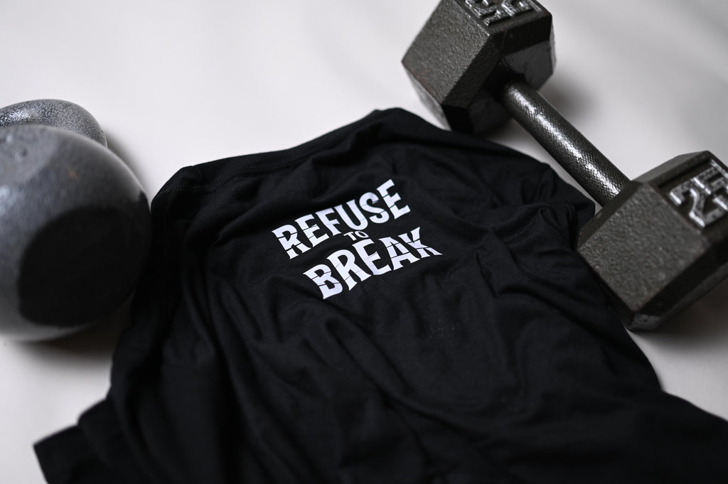Black t-shirt with 'REFUSE to BREAK' text, lying on a white surface with dumbbells.