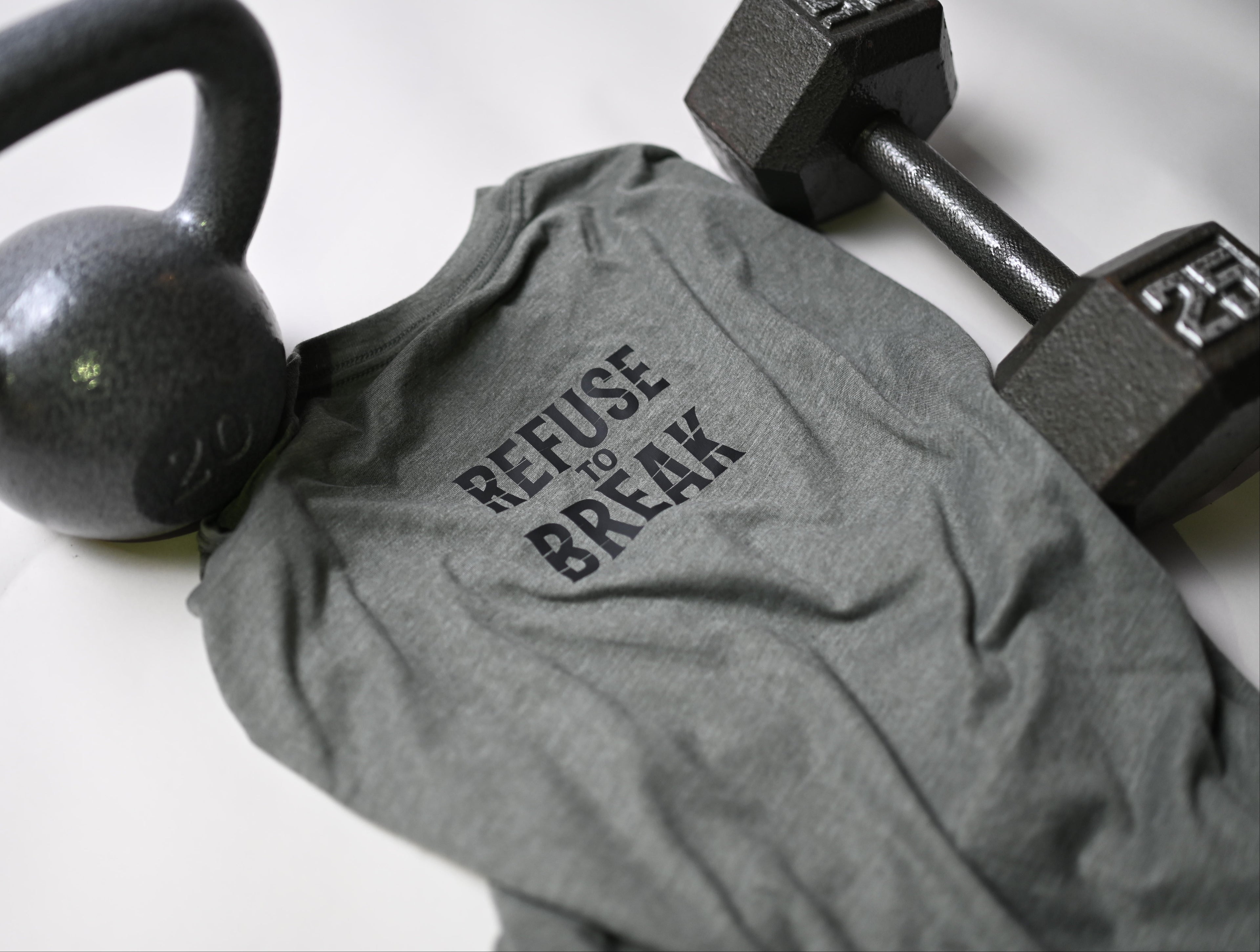 Gray t-shirt with 'Refuse to Break' text, kettlebell, and dumbbells on a light background