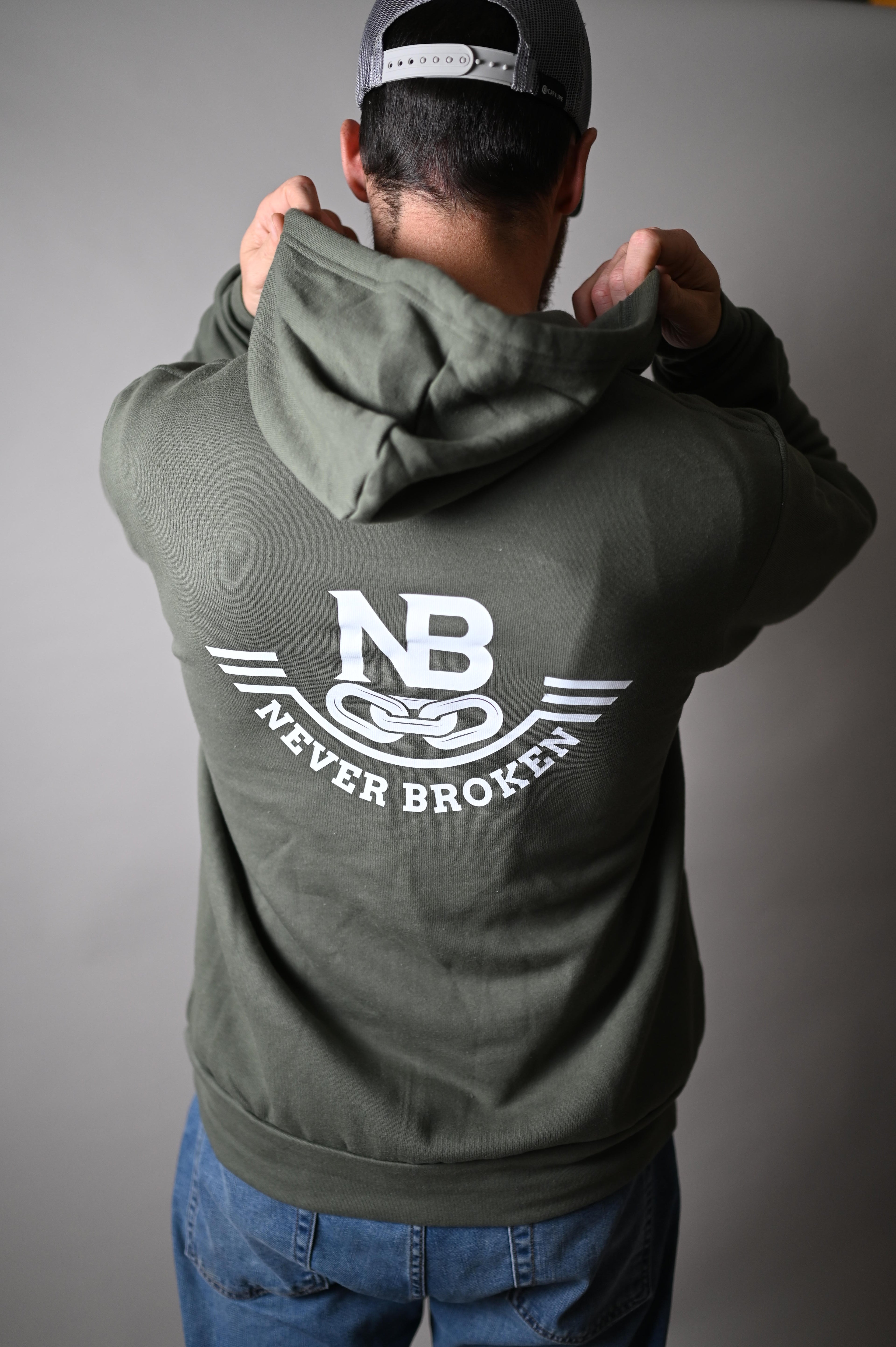 Person wearing a green hoodie with 'Never Broken' logo on a gray background