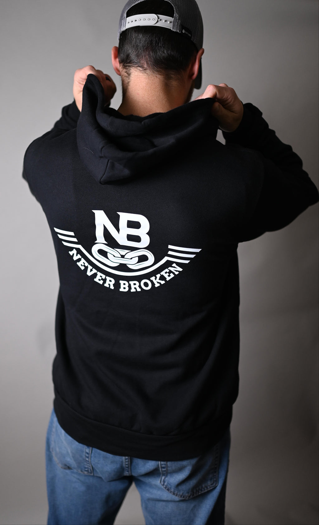 Person wearing a black hoodie with a logo, standing against a gray background