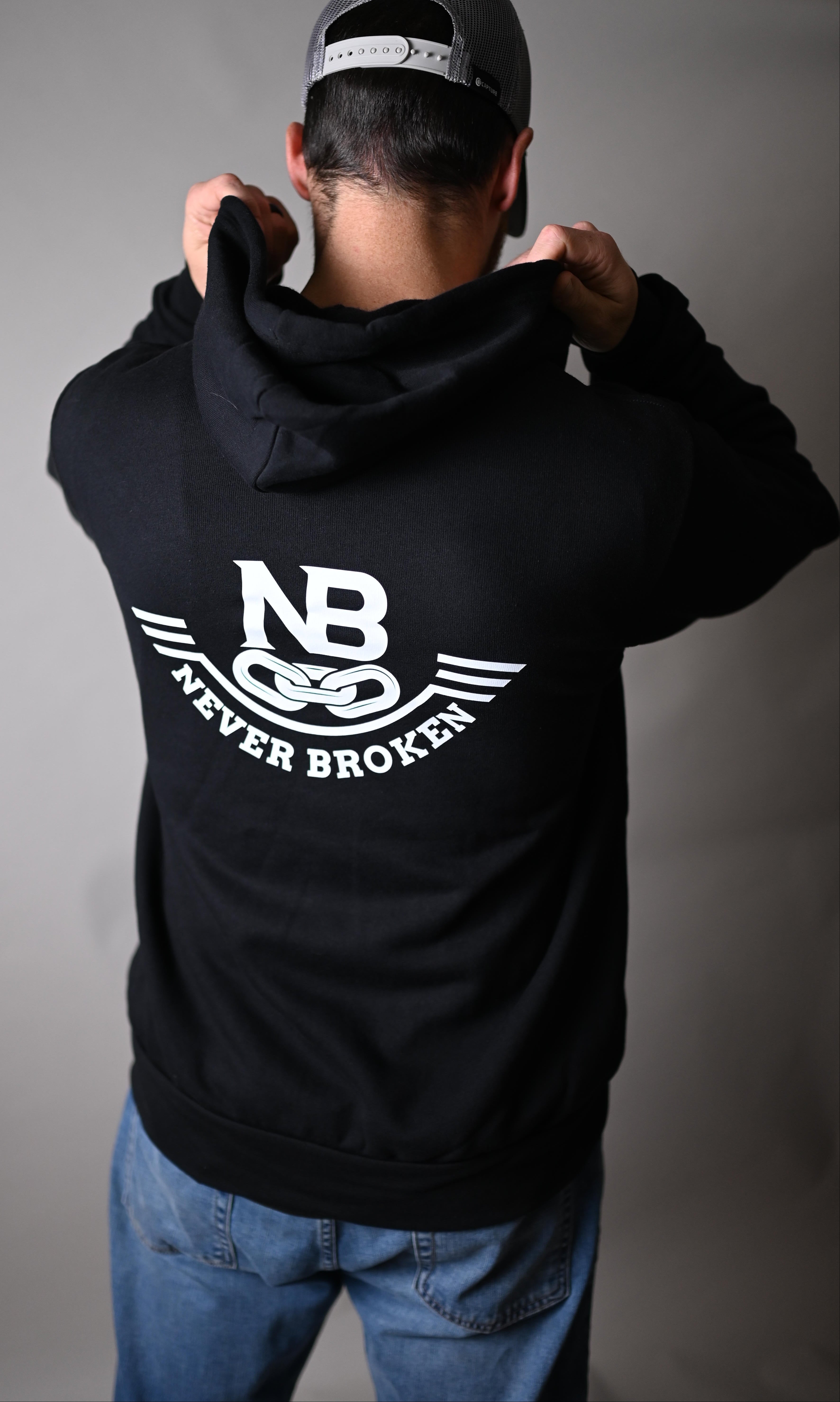 Person wearing a black hoodie with a logo, standing against a gray background