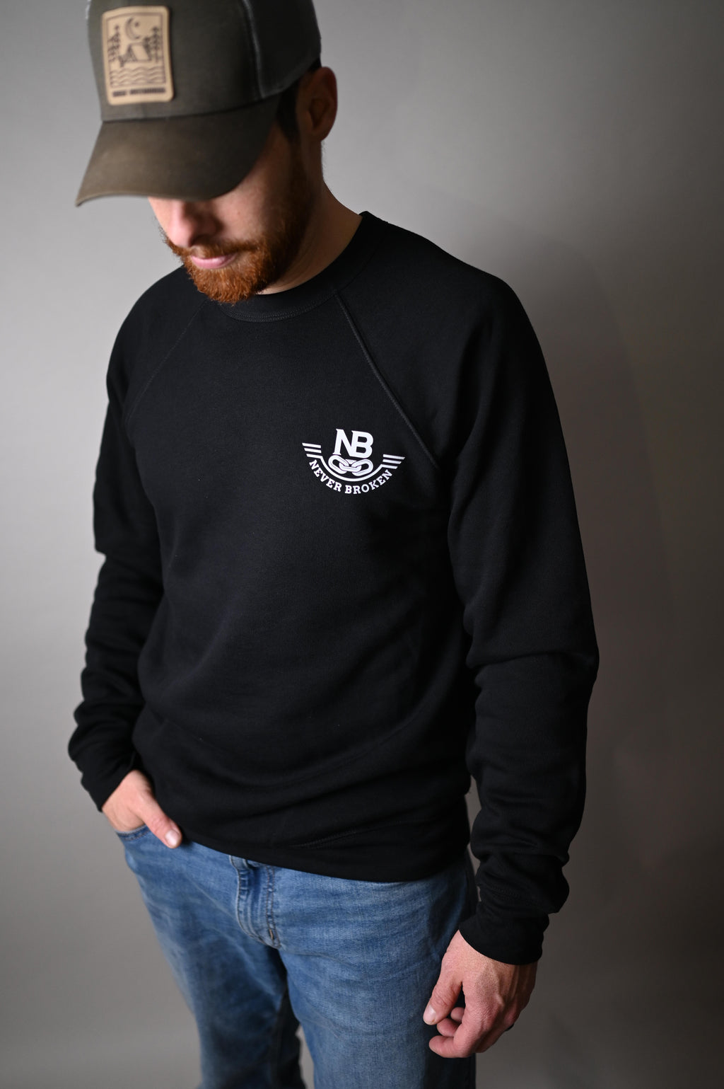 Person wearing a black hoodie with a logo and a cap on a gray background