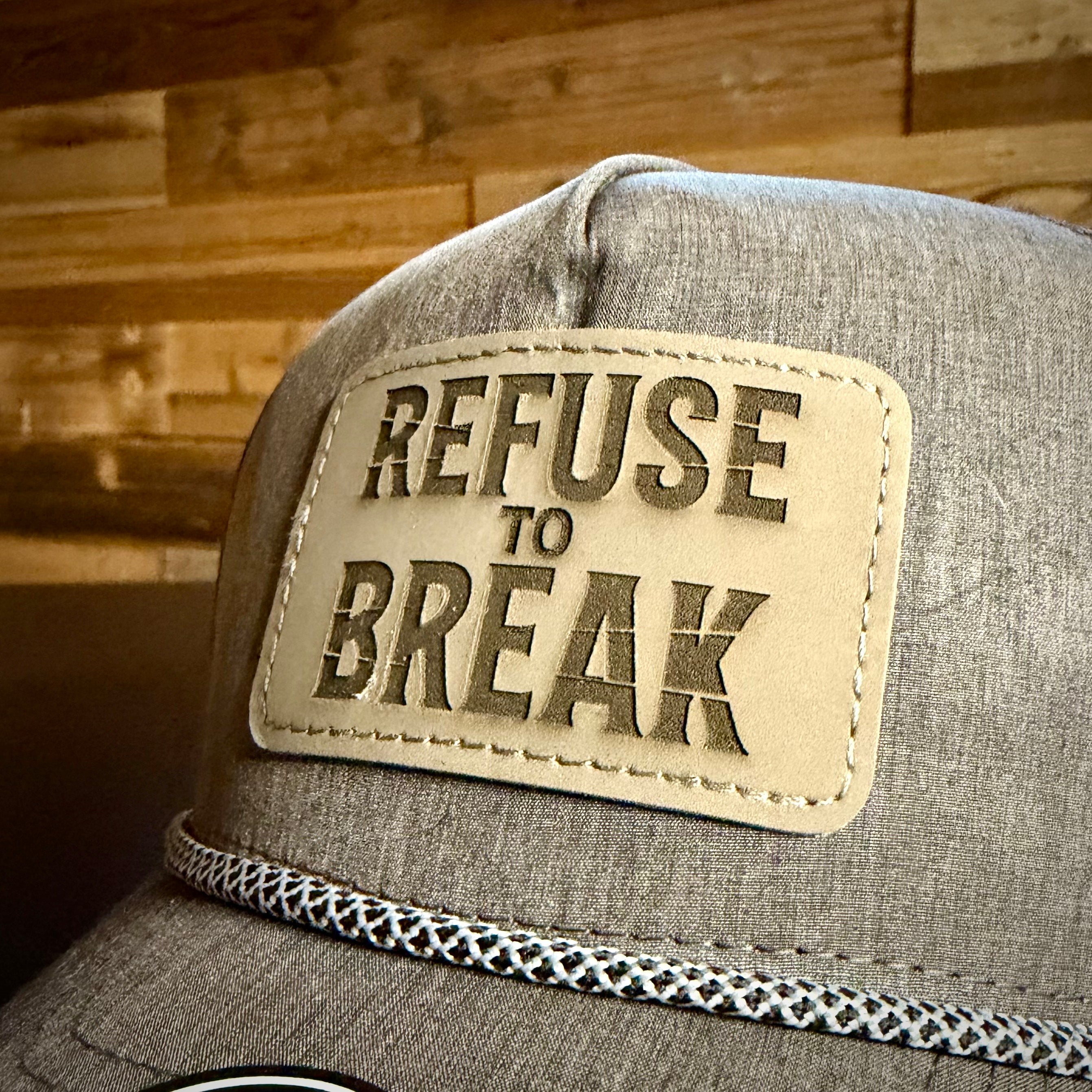 Gray cap with a leather patch reading 'Refuse to Break' against a wooden background